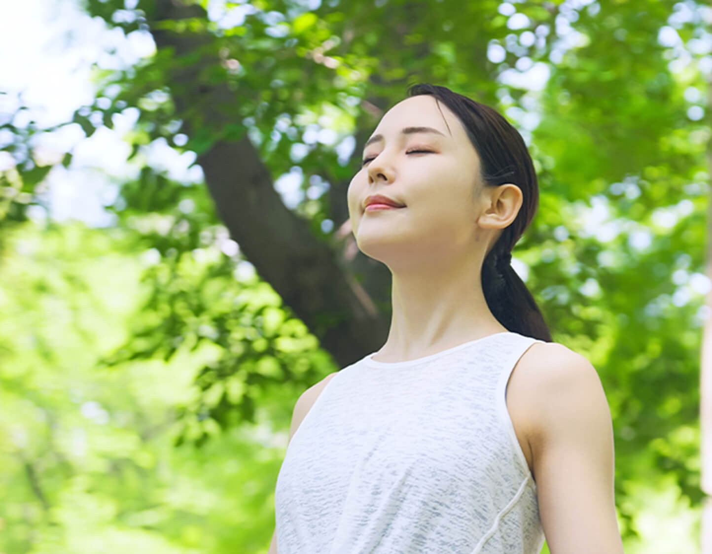 緑の木の下で、目を瞑って深呼吸している女性